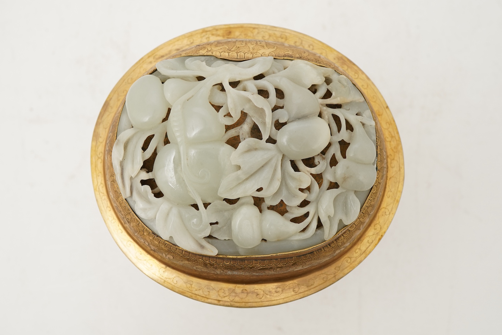A Chinese pale celadon jade oval plaque, 17th/18th century, mounted on a late Qing gilt copper jar